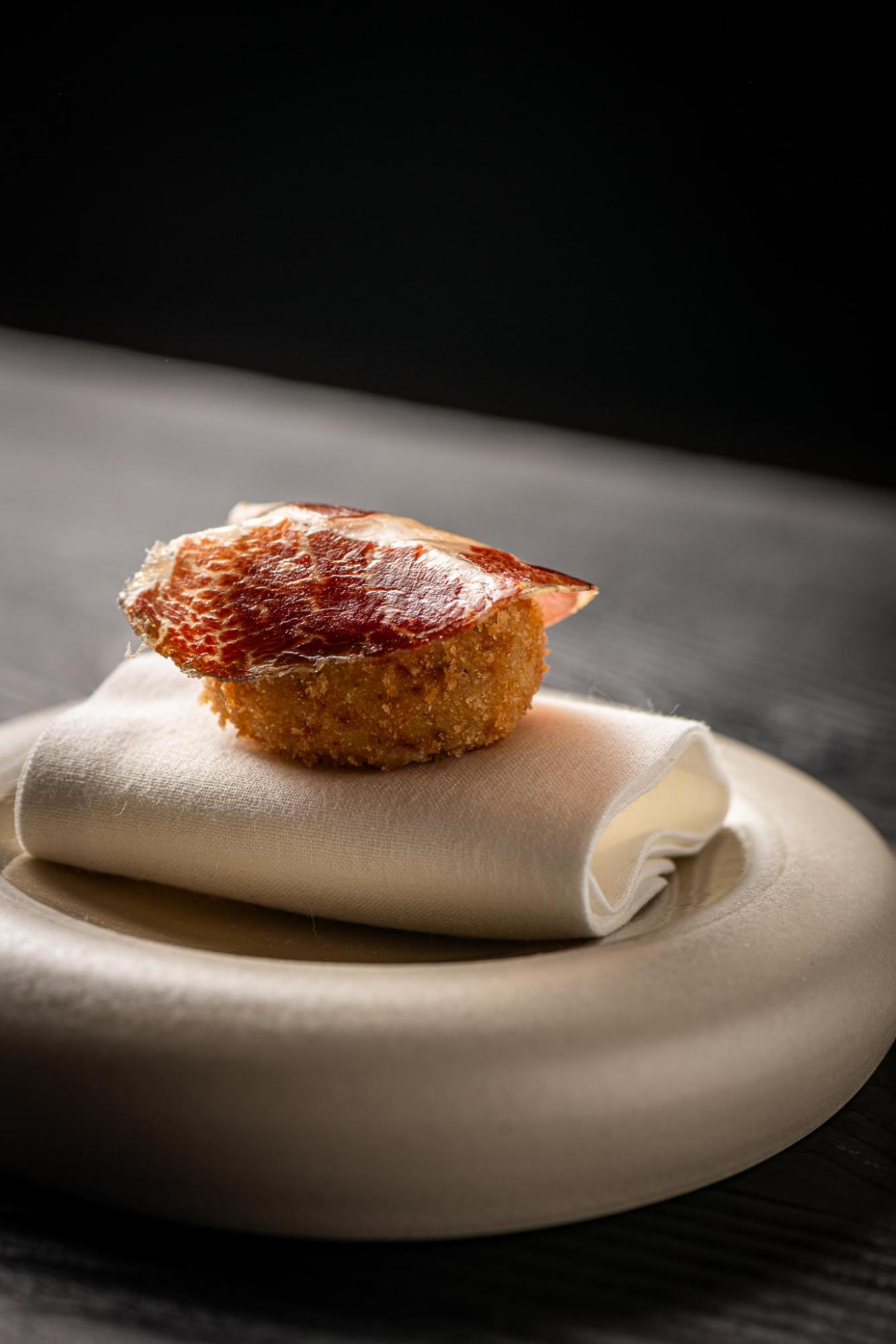 Una croqueta se presenta sobre una servilleta blanca sobre una bandeja.