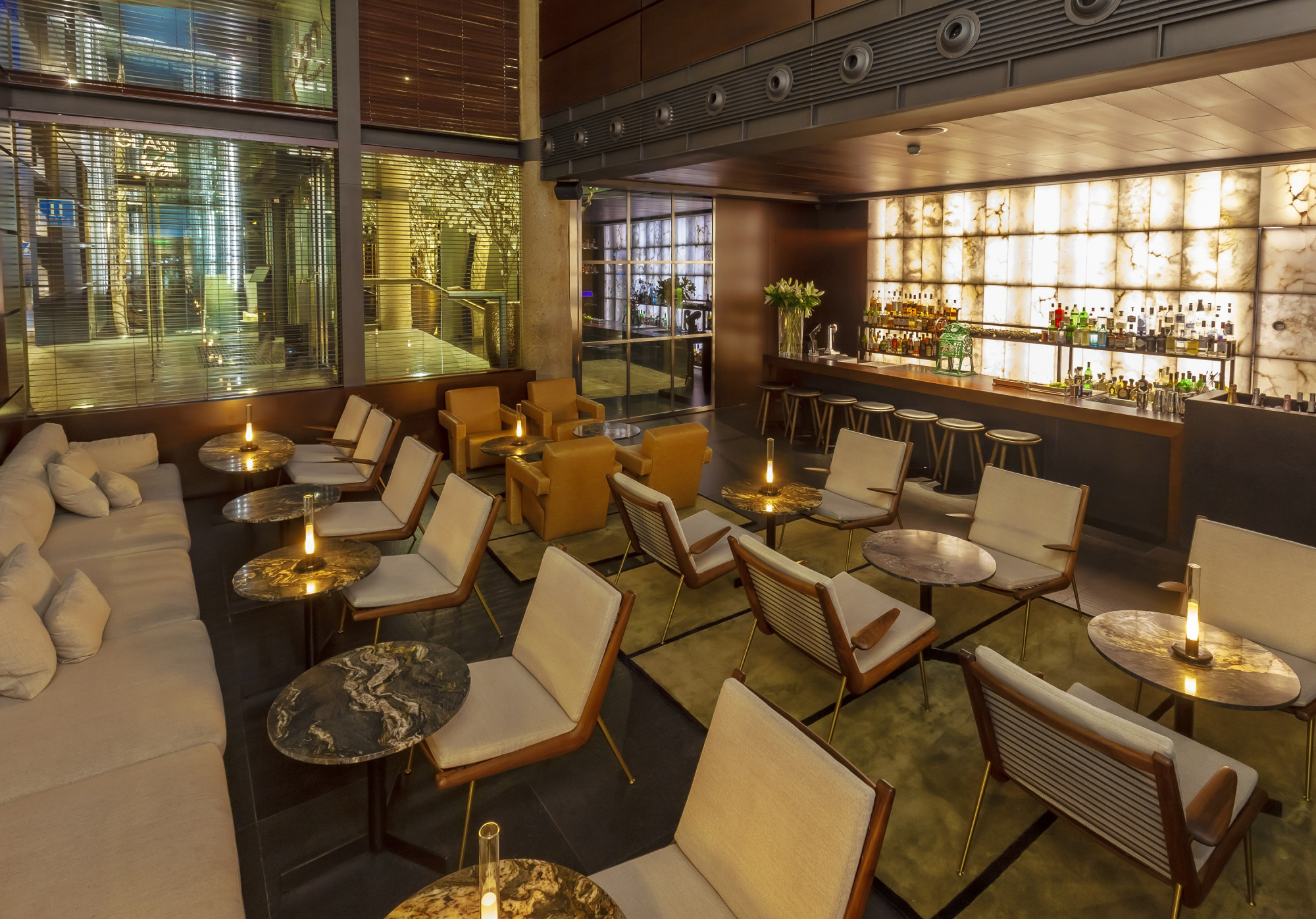 Se ve una terraza interior con mesas, sillas y velas encendidas junto a una barra iluminada.