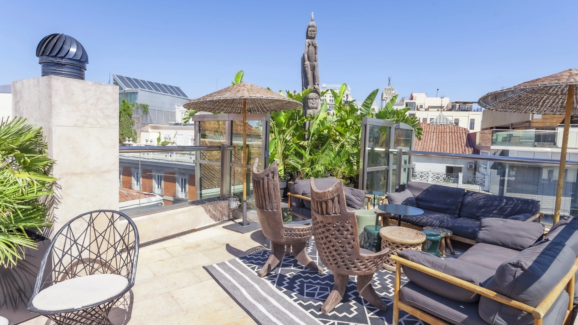 Se ve una terraza en la azotea con tumbonas, mesas y barandillas de vidrio bajo el cielo despejado.