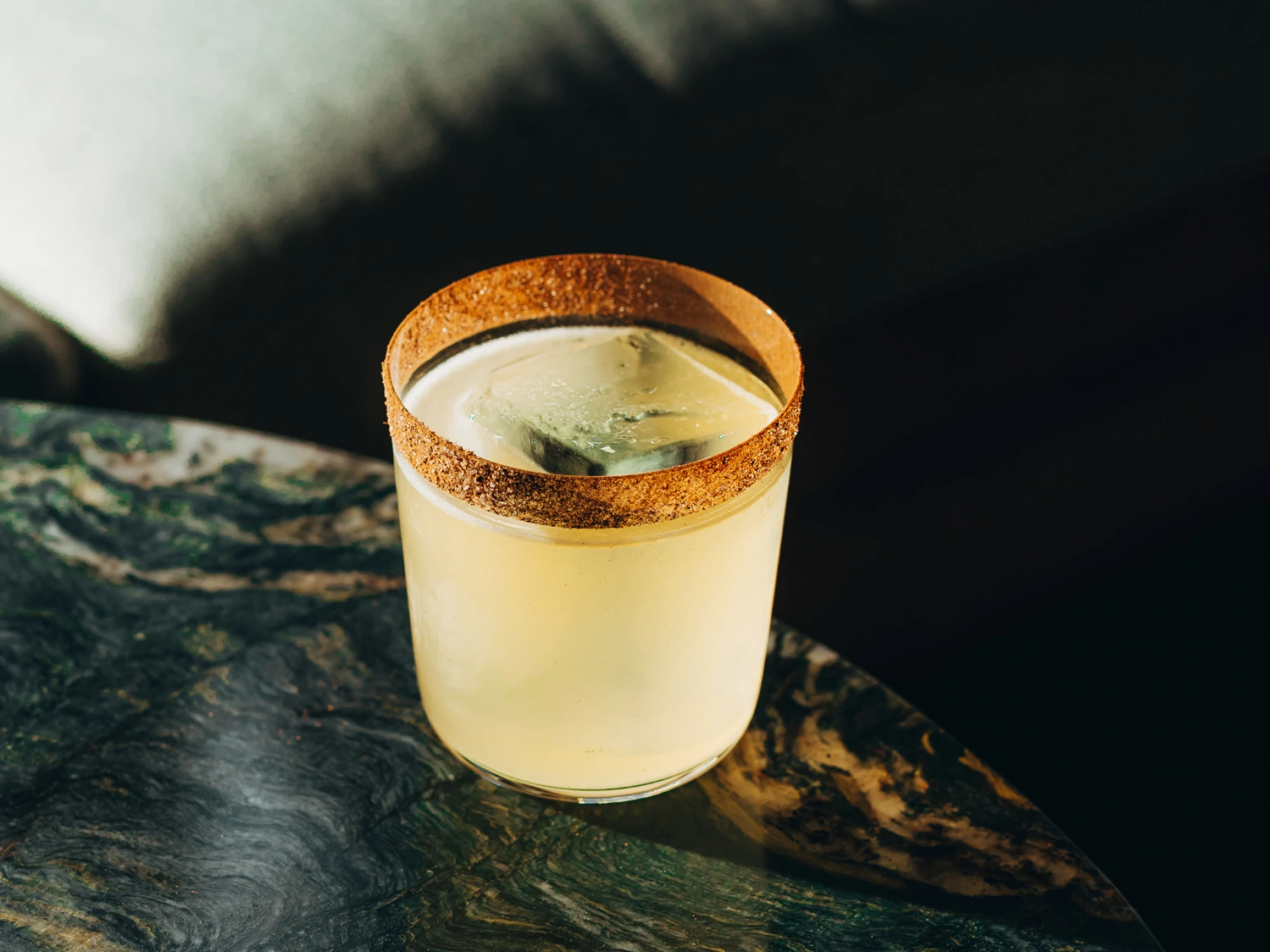 Sirven una copa con cocktail Margarita sobre una superficie oscura.