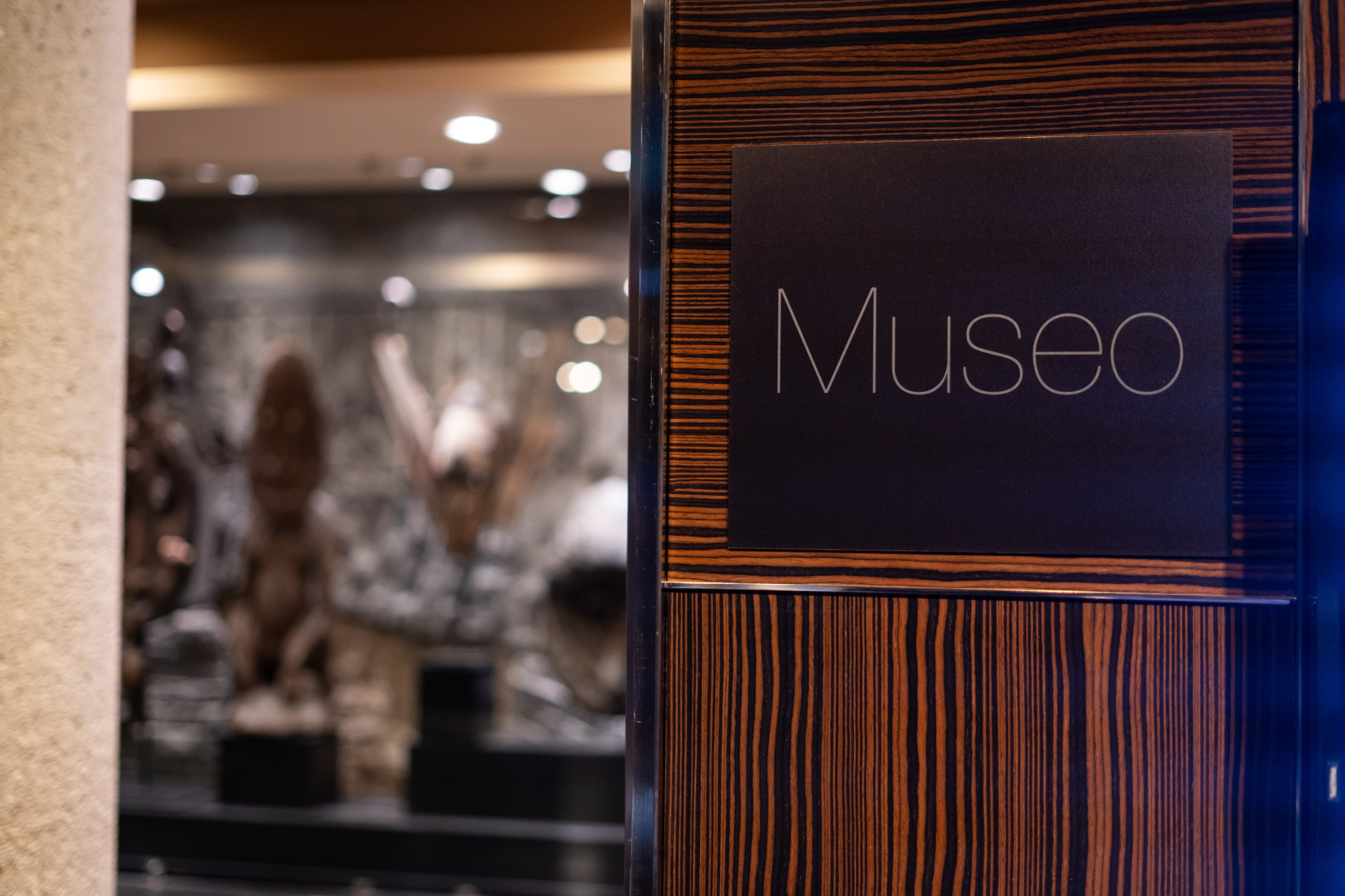 Se ve un letrero con la palabra “Museo” junto a una pared de madera y un espacio interior al fondo.