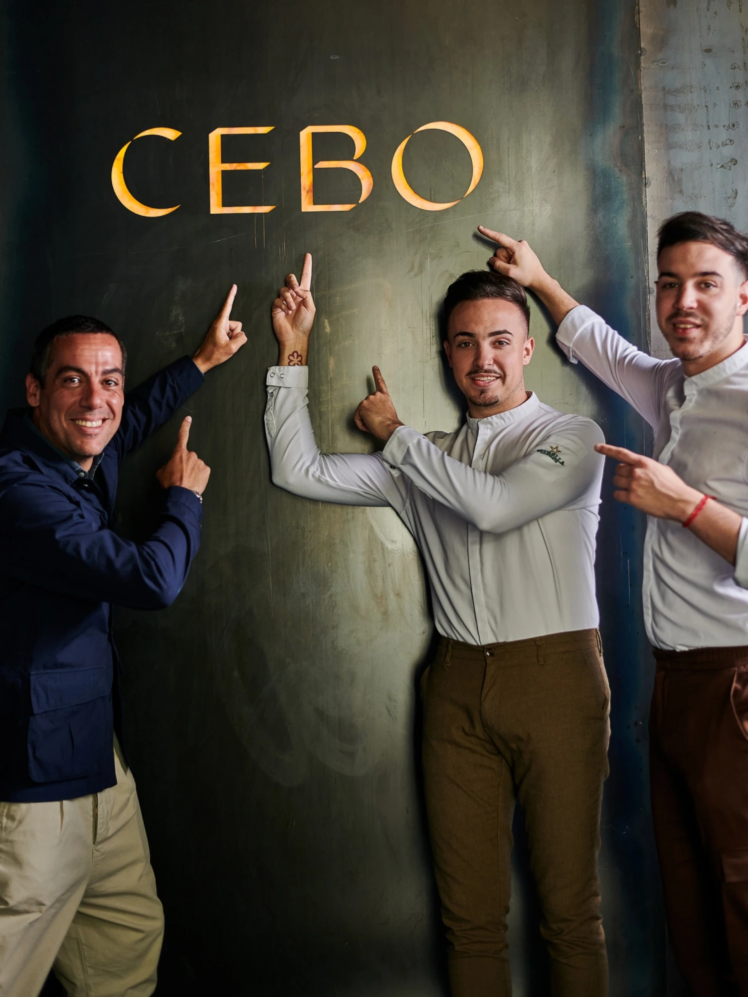 Un grupo de personas posa delante de un letrero luminoso que dice “CEBO”.