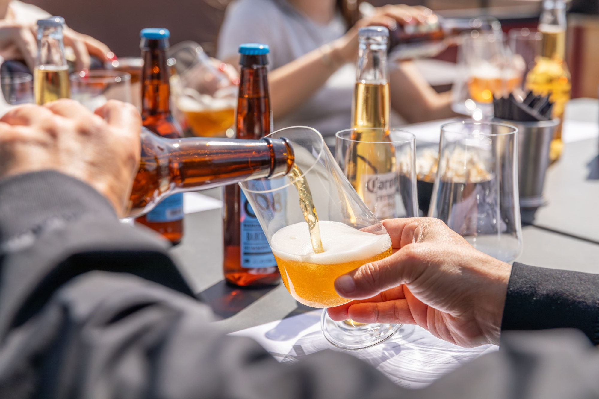 Mehrere Personen stoßen mit Biergläsern an einem Tisch mit Flaschen und Gläsern an.