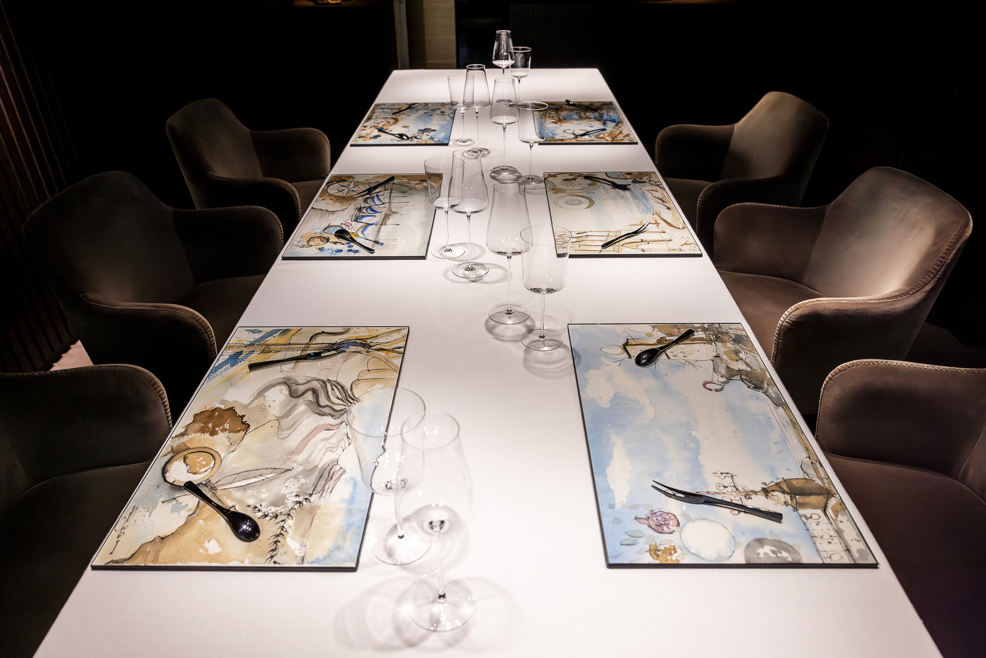 Se ve una mesa larga con mantelería y vajilla, rodeada de sillas tapizadas en un comedor.