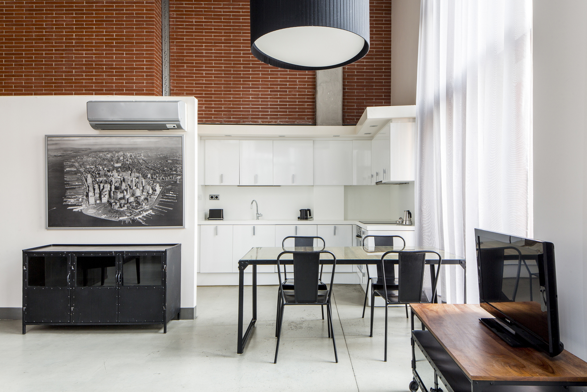 Se ve una cocina con barra y taburetes junto a una mesa de trabajo en un espacio interior luminoso.