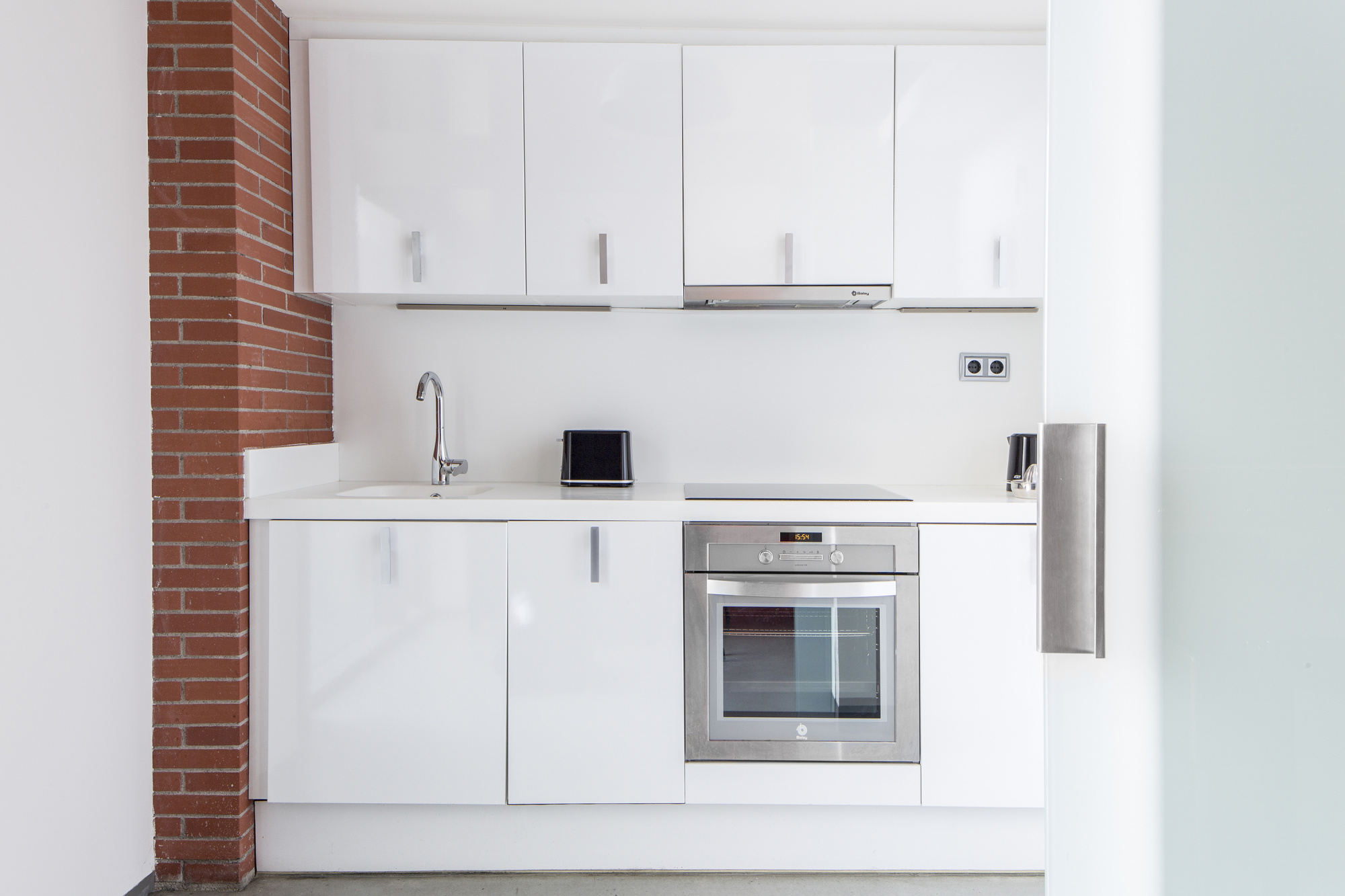 Cocina blanca con encimera, fregadero y horno empotrado bajo armarios superiores.