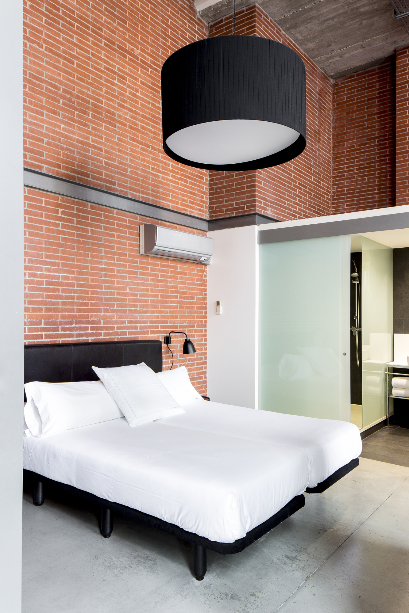 Un dormitorio con cama doble, pared de ladrillo y luz de techo sobre el cabecero.