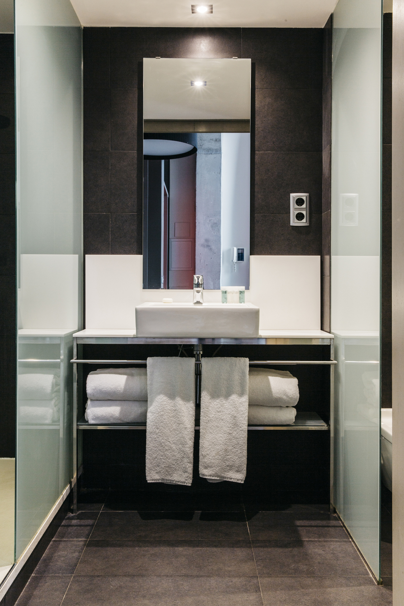Se ve un baño moderno con lavabo sobre mueble, espejo y toallas dobladas.