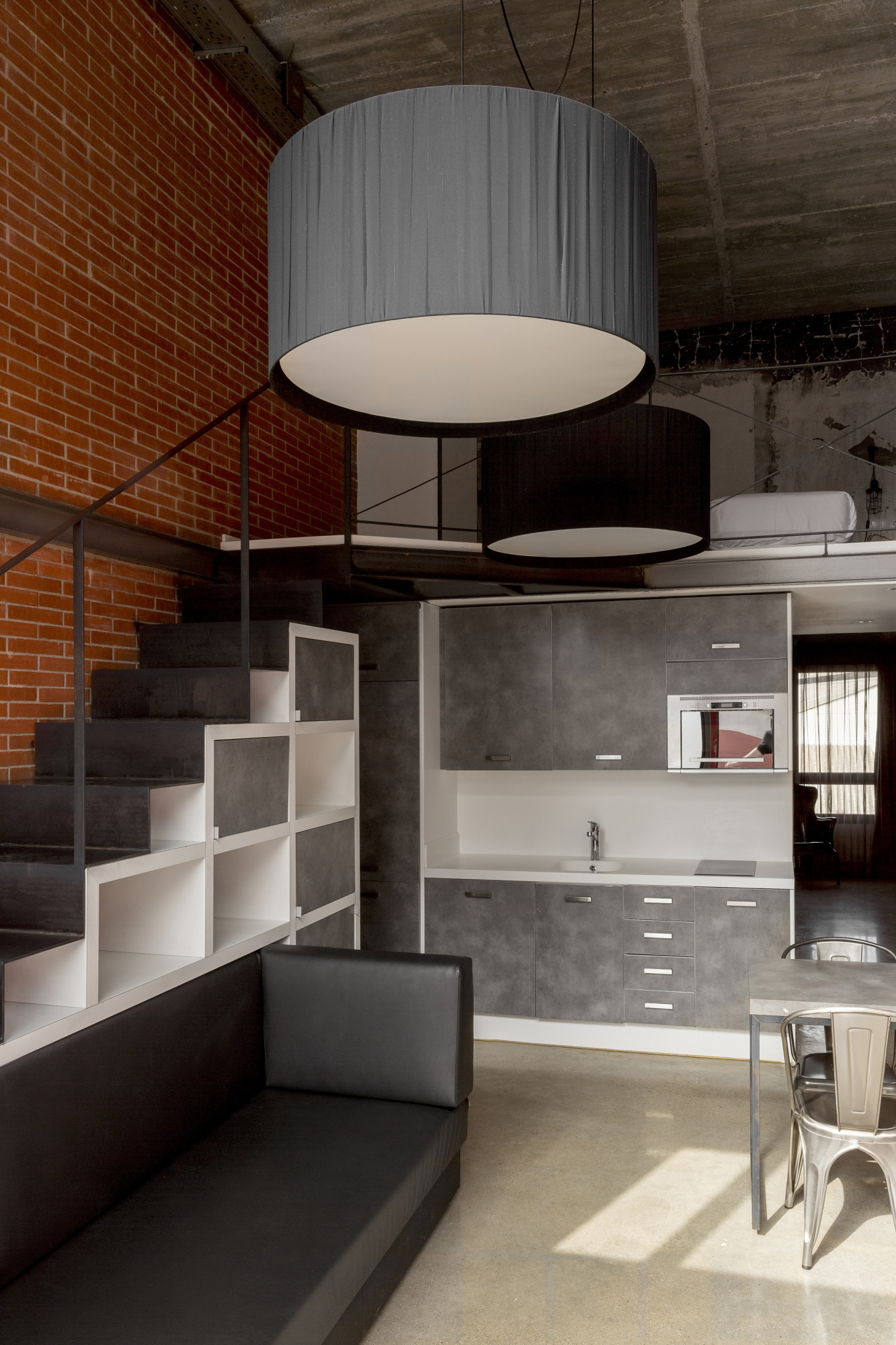 Se ve una cocina moderna con encimera de hormigón, barra y estantería decorativa, con luz empotrada y lámpara colgante.