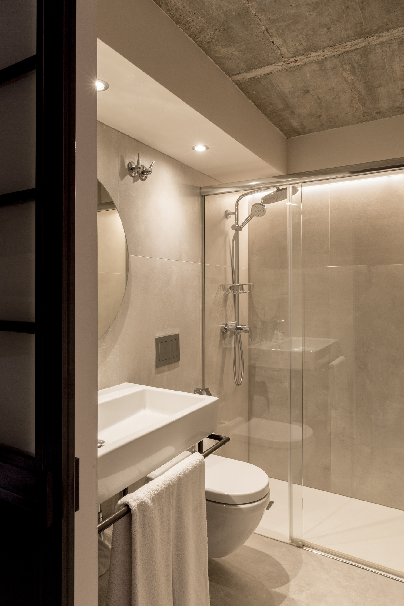 Se ve un baño moderno con ducha de lluvia, bañera empotrada, inodoro y paredes revestidas en tonos claros.