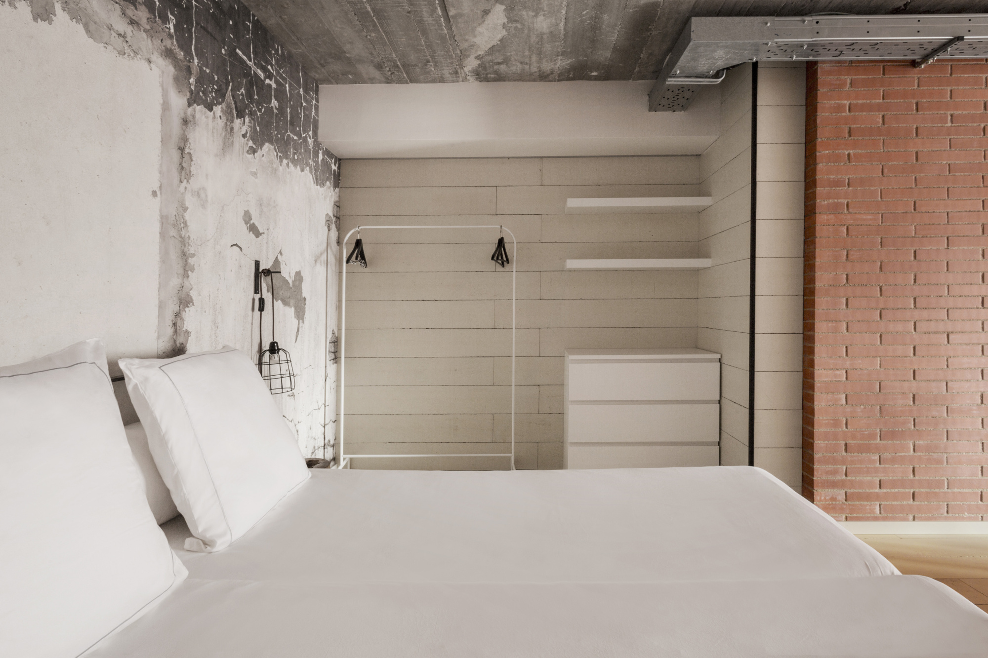 Se ve una cama con ropa de cama blanca y un armario empotrado con estantes y colgadores.