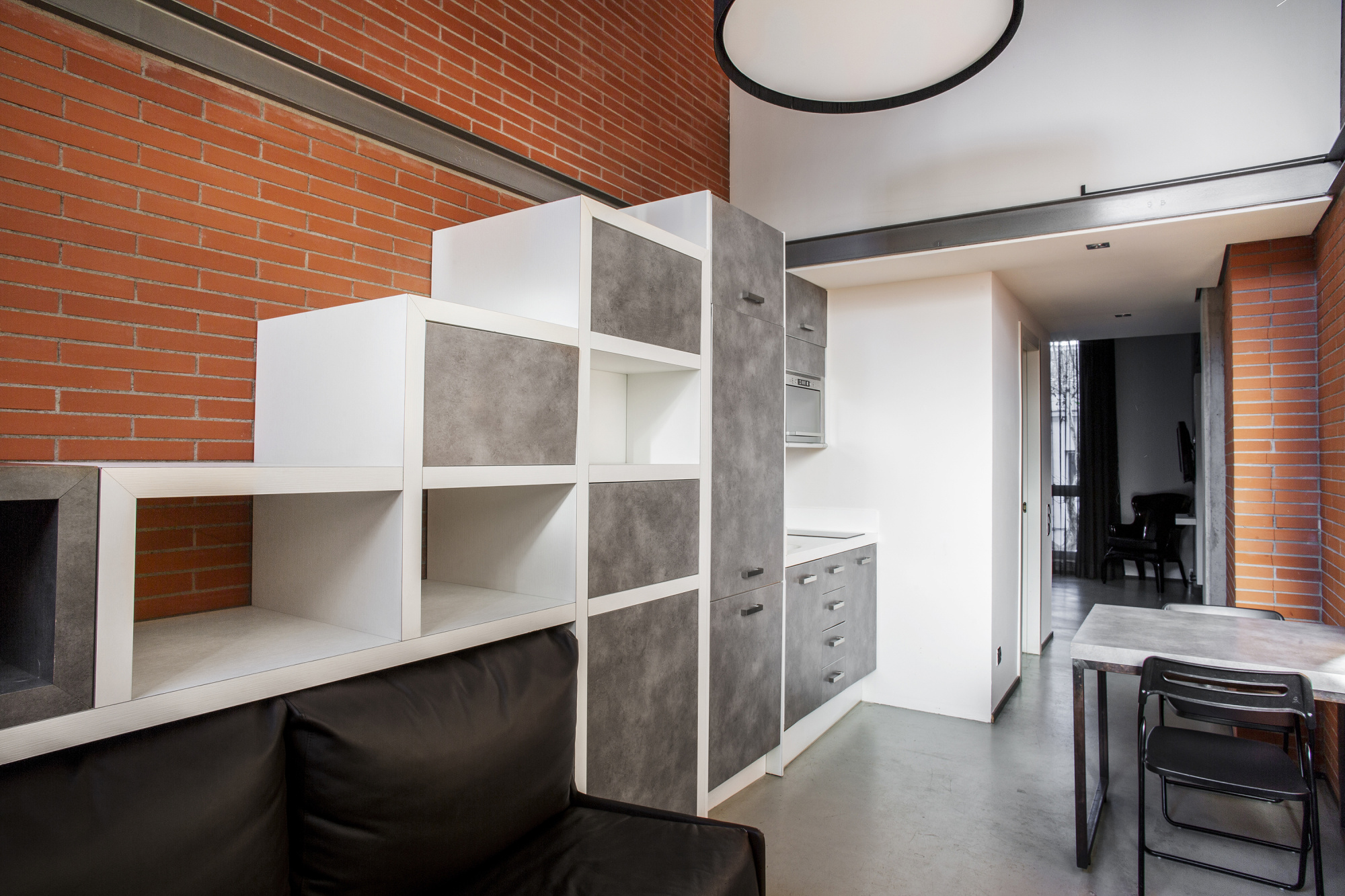 Se ve una zona de estar con un librero modular blanco y un pequeño escritorio junto a una pared de ladrillo.