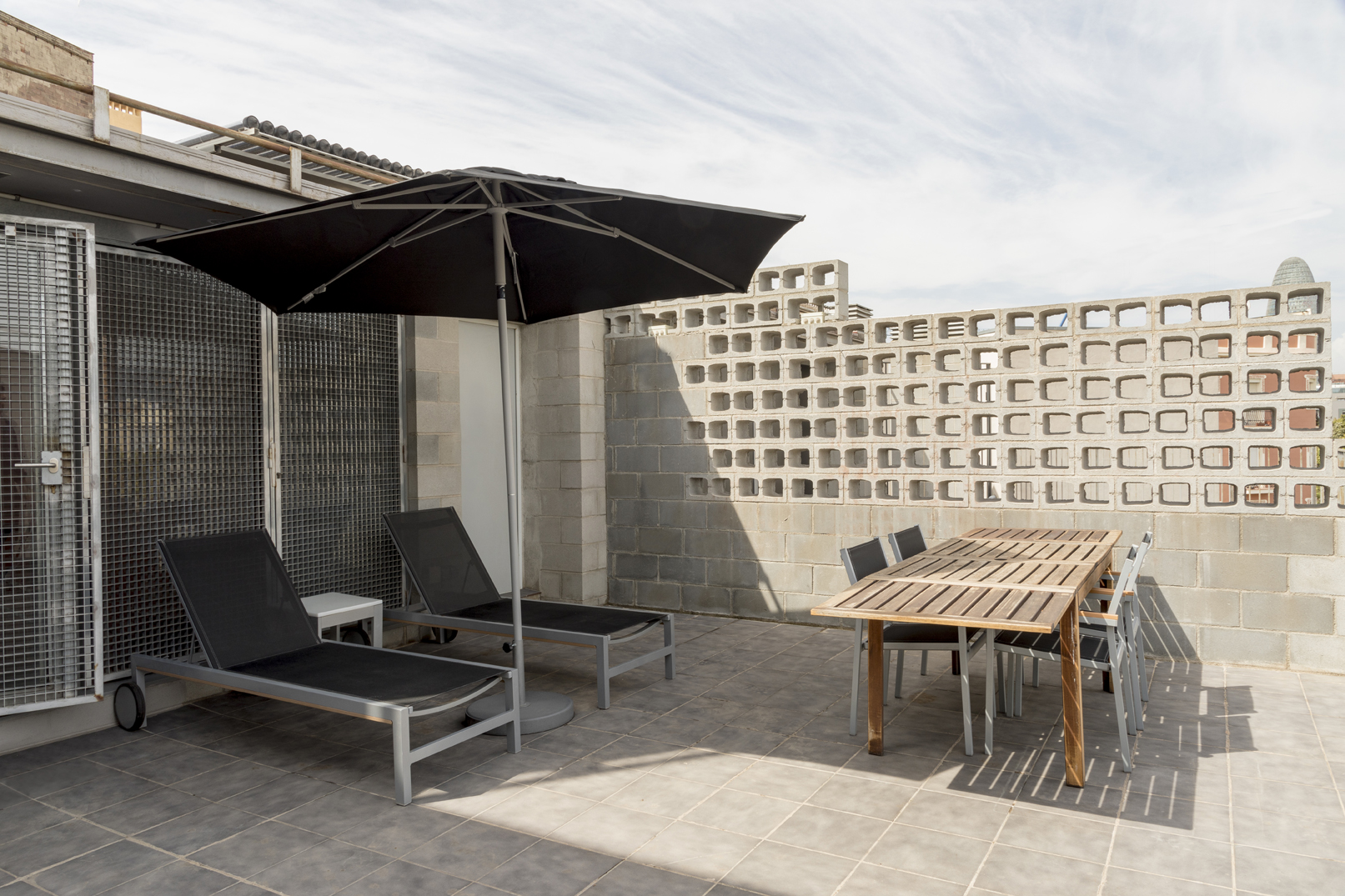 Se ve una terraza exterior con una tumbona doble, una mesa de madera y suelos de baldosa.