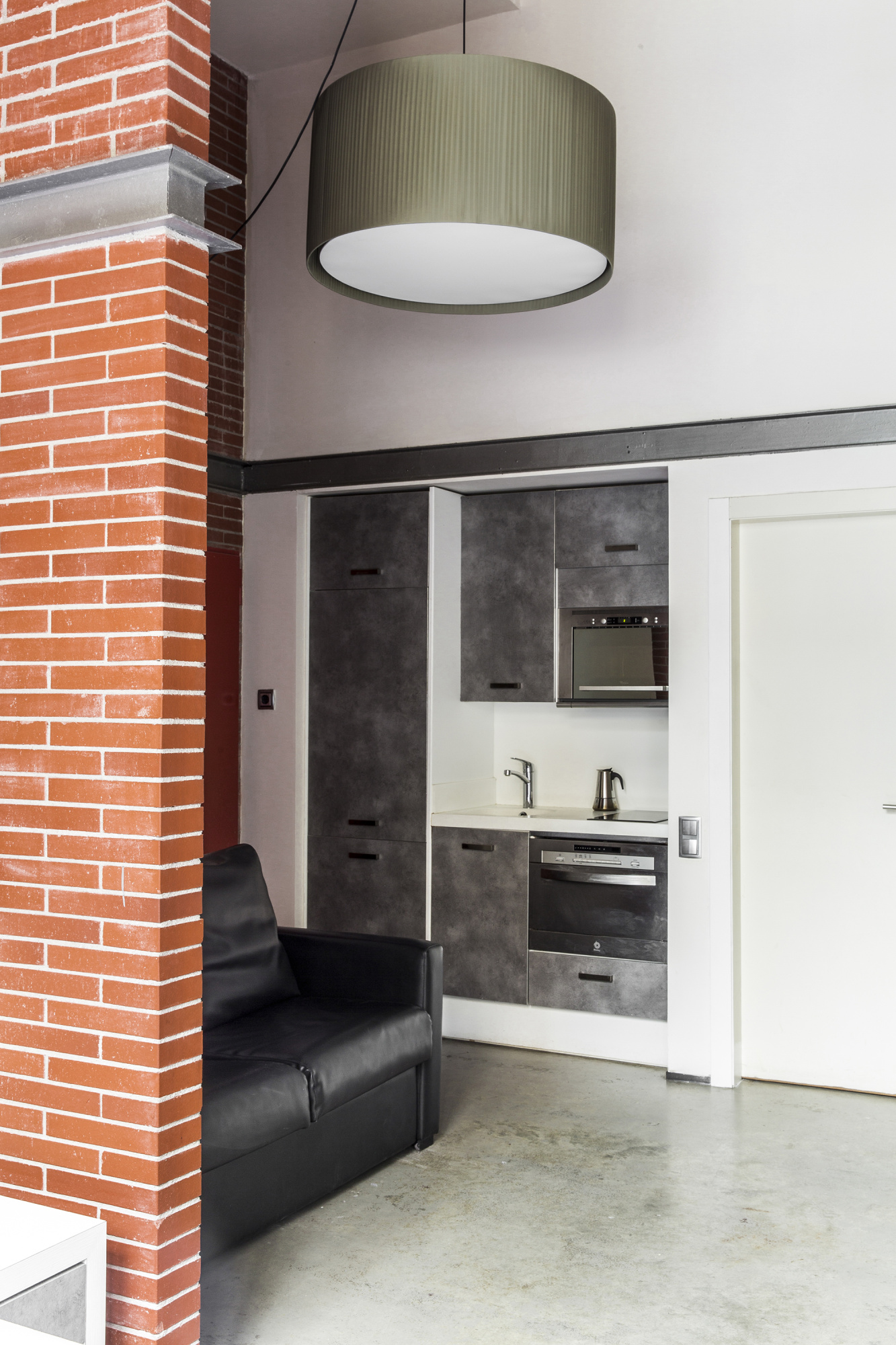 Se ve una zona de estar con sofá y una cocina integrada con encimera y horno empotrado.