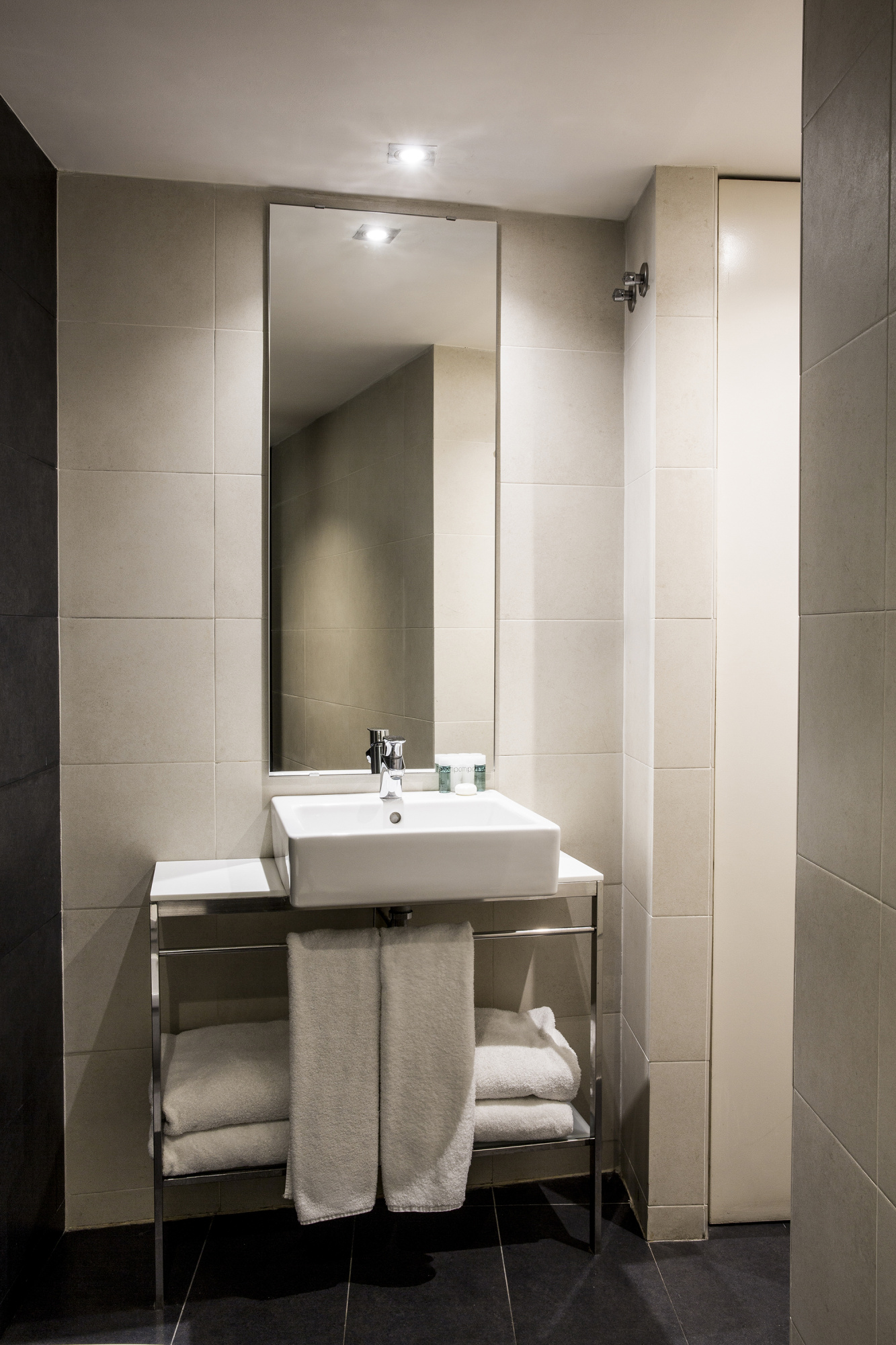 Se ve un baño moderno con lavabo, espejo y toallas sobre un soporte.