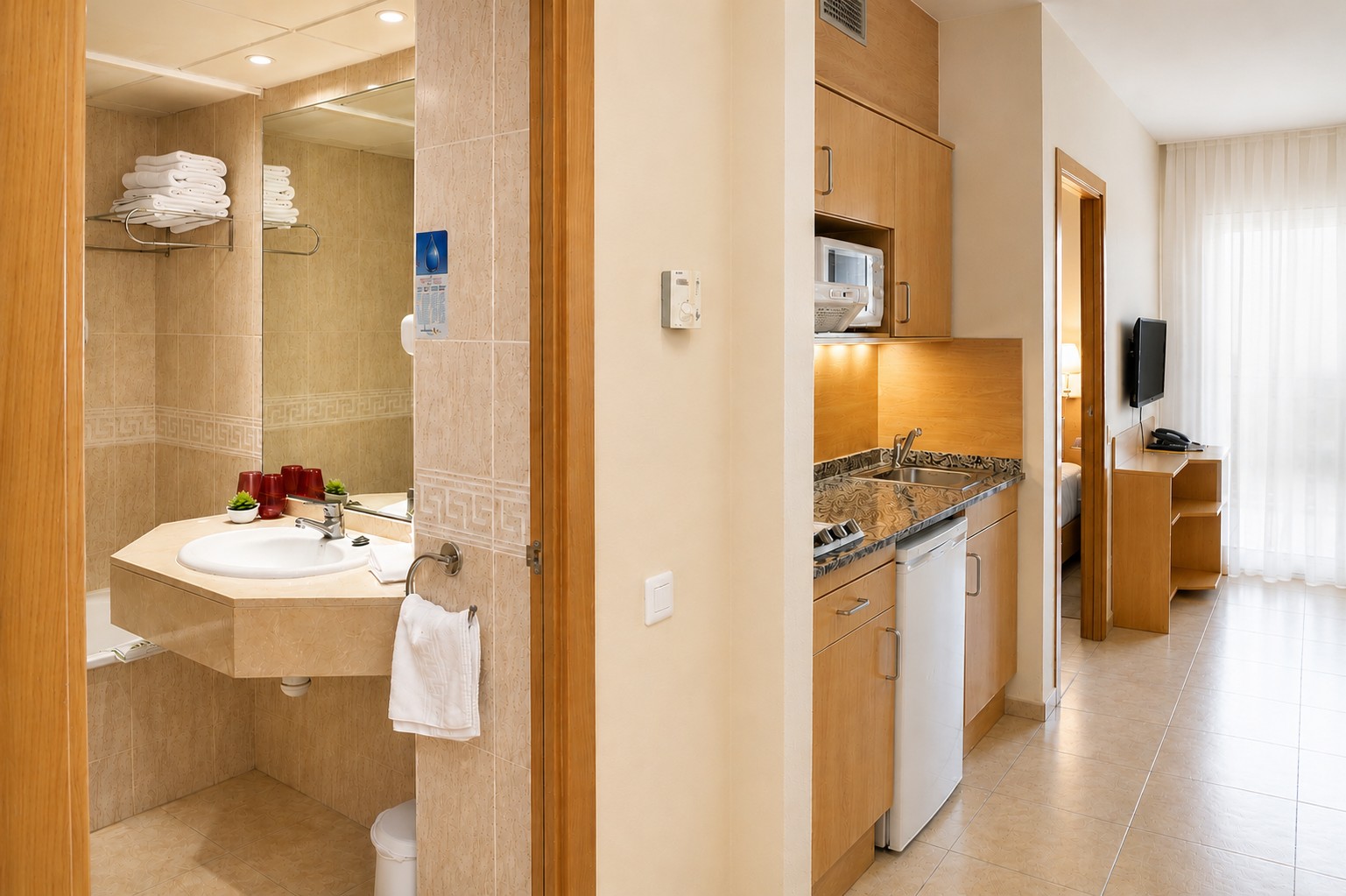 Se ve un baño con lavabo y ducha, y una cocina integrada con encimera y electrodomésticos junto a una zona de estar.