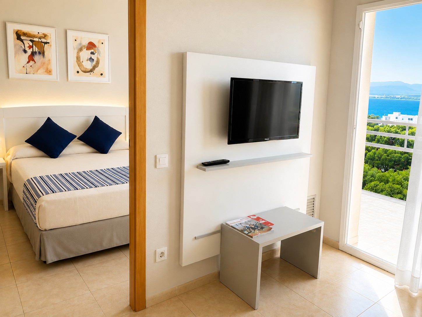 Se ve una sala con televisor de pantalla plana, mesa auxiliar y una zona de descanso con sofá y cama.