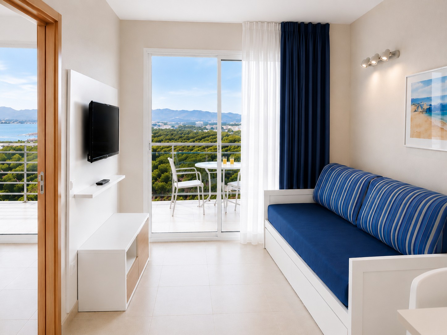 Se ve una habitación con cama, televisor y acceso a una terraza con barandilla y vistas al paisaje.