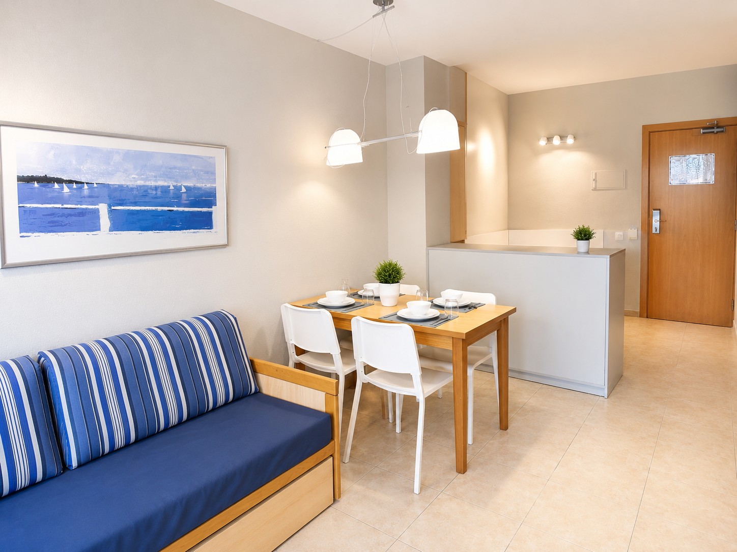 Se ve una sala con sofá azul, mesa de comedor con sillas y una cocina abierta con barra blanca.