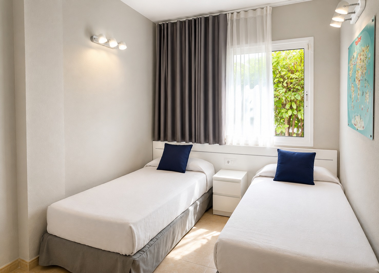 Se ve un dormitorio con dos camas individuales, cortinas oscuras y una ventana con luz natural.