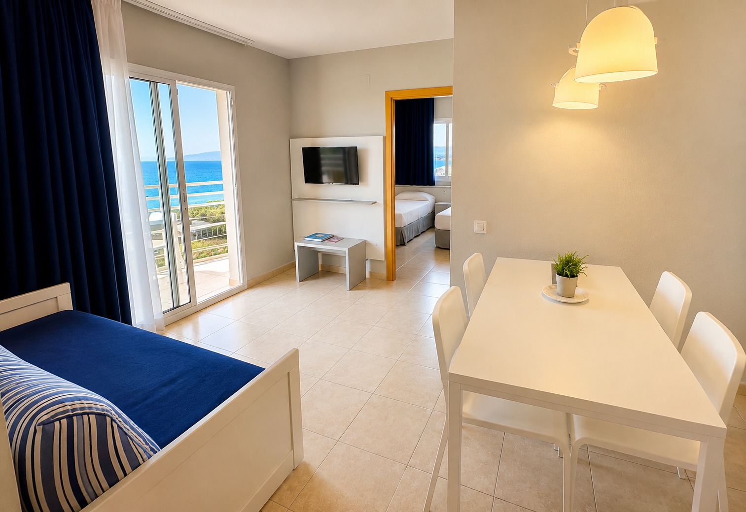 Se ve una habitación con cama, mesa blanca, televisión y una puerta con salida a balcón con vista al mar.