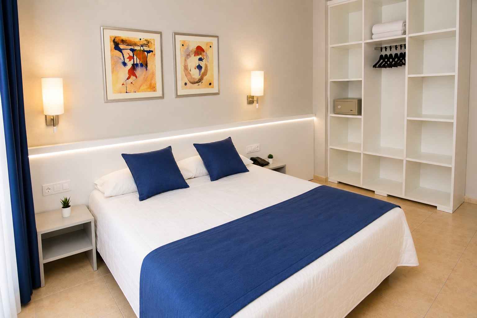 Se ve una cama con ropa de cama blanca y azul, mesitas laterales y estanterías empotradas en la pared.