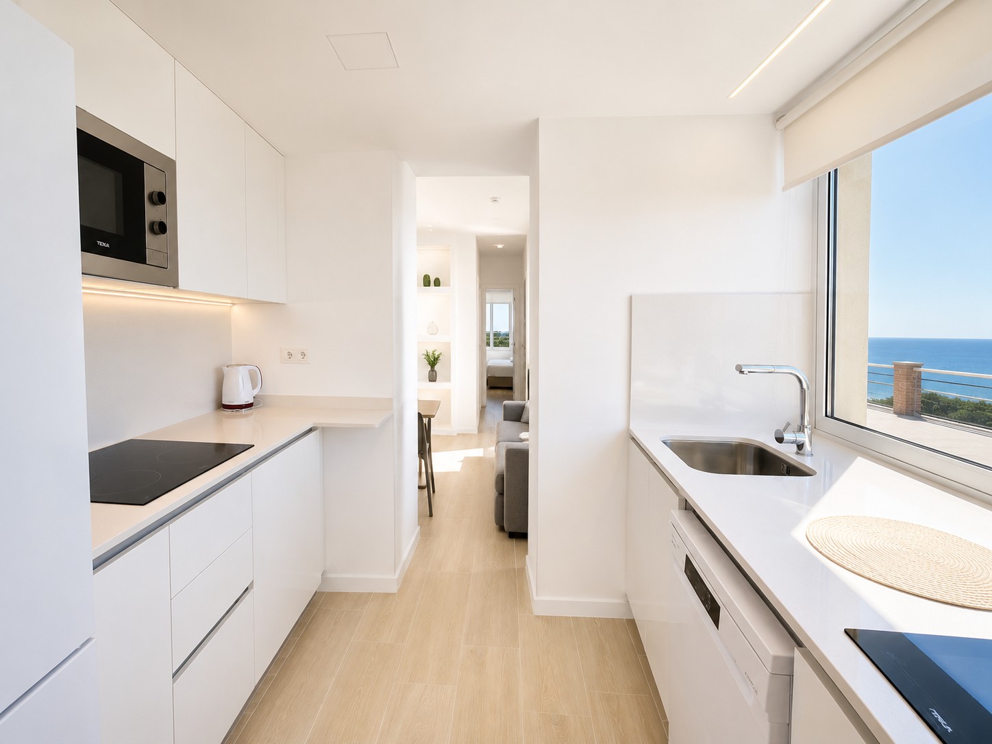 Cocina moderna blanca con encimera, fregadero y ventana con vista al mar.