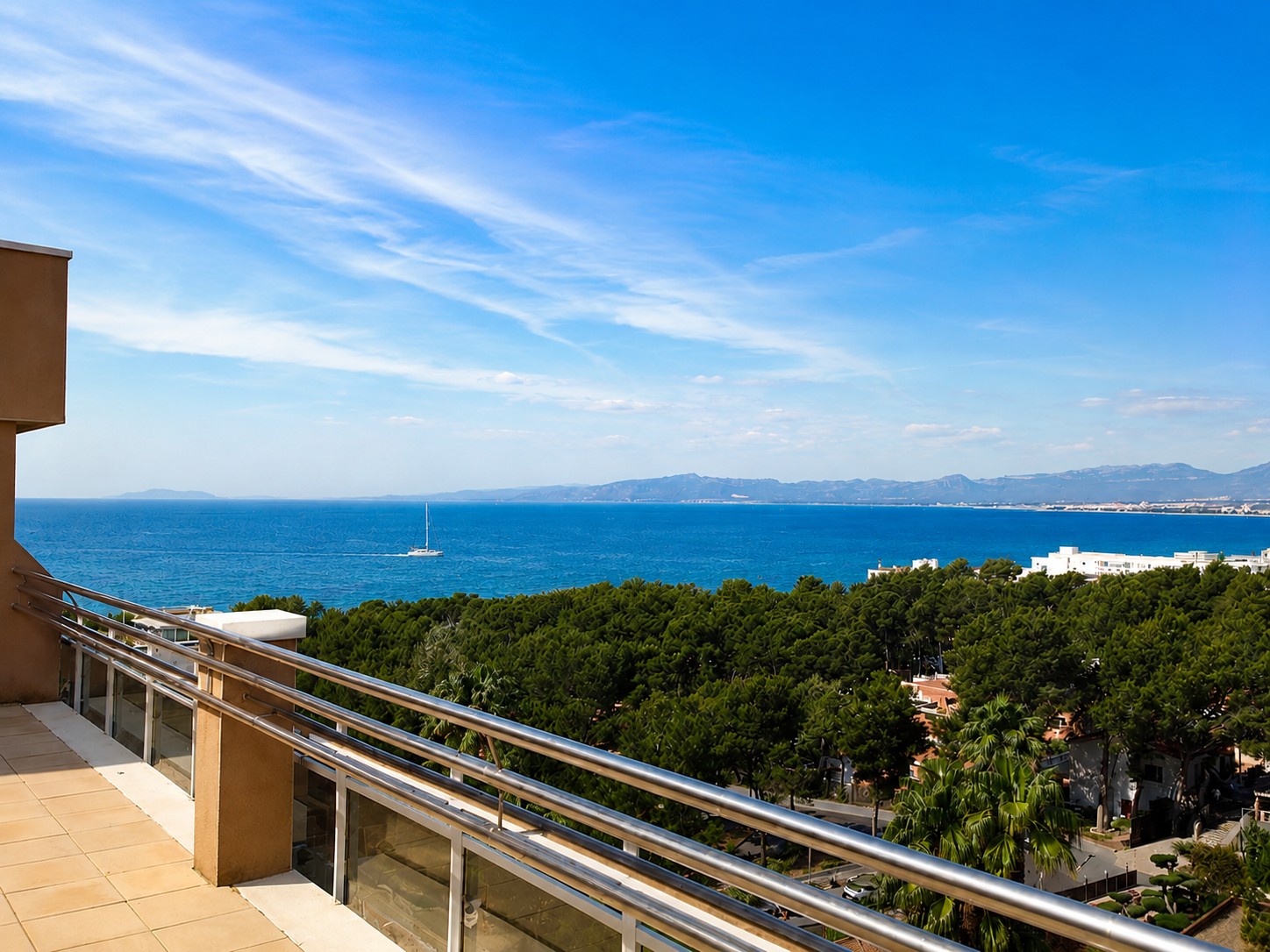 Desde la terraza se ve el mar y la costa a lo lejos, con barandilla y suelo de baldosas.