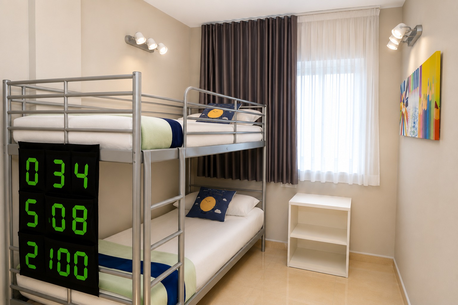 Se ve una habitación con literas metálicas, una mesita y una ventana con cortinas.