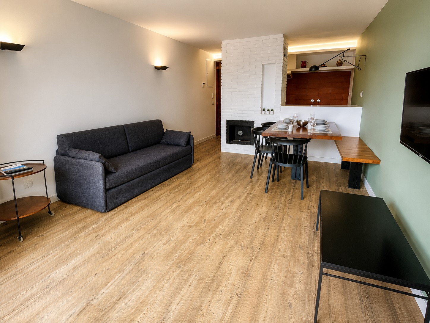Se ve una sala con sofá gris, mesa de comedor y cocina integrada con barra.