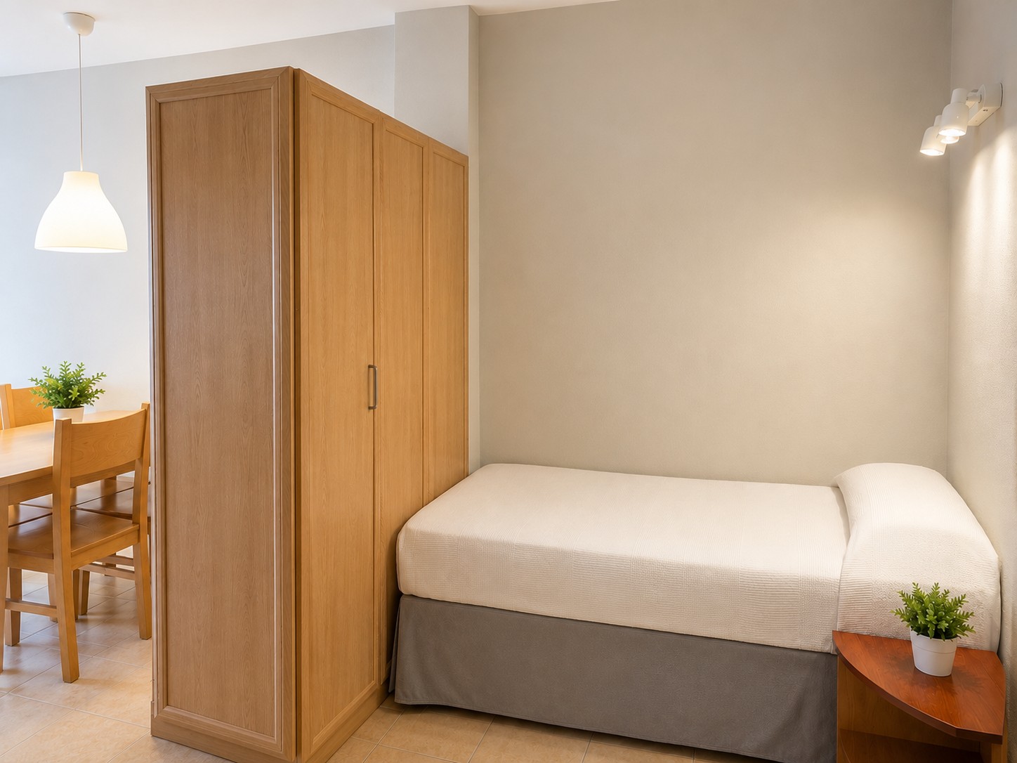 Se ve una cama individual con un armario de madera y mesita con macetas decorativas.