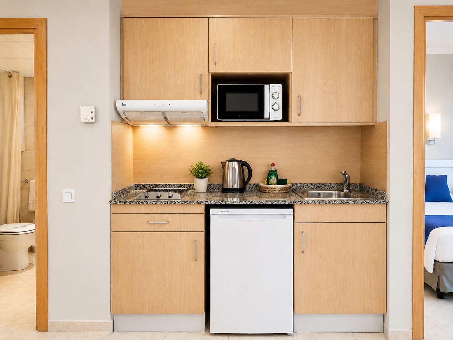 Se ve una cocina compacta con encimera, fregadero, microondas y hervidor eléctrico sobre el mueble.