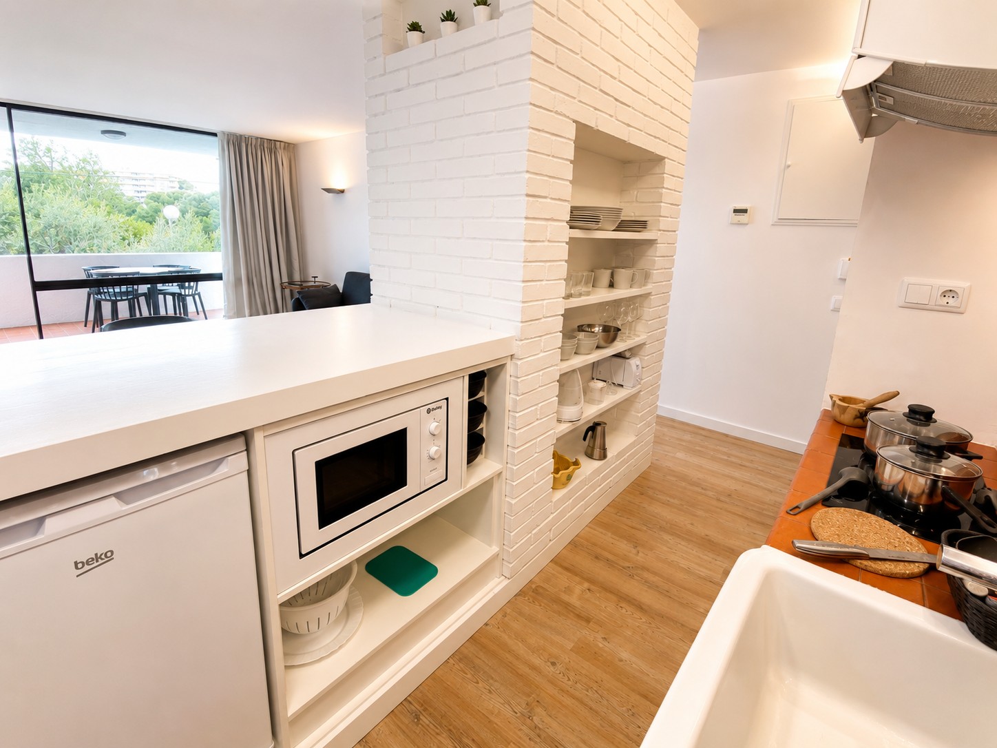 Se ve una cocina equipada con microondas empotrado, encimera blanca y utensilios sobre la zona de preparación.