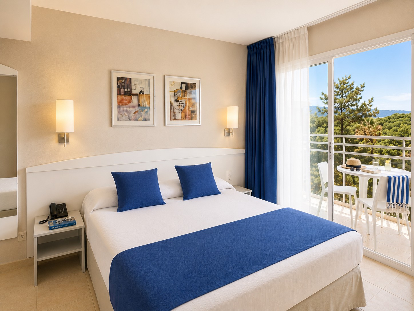 El dormitorio muestra una cama con ropa blanca y cojines azules, lámparas de pared y una puerta al balcón con barandilla.