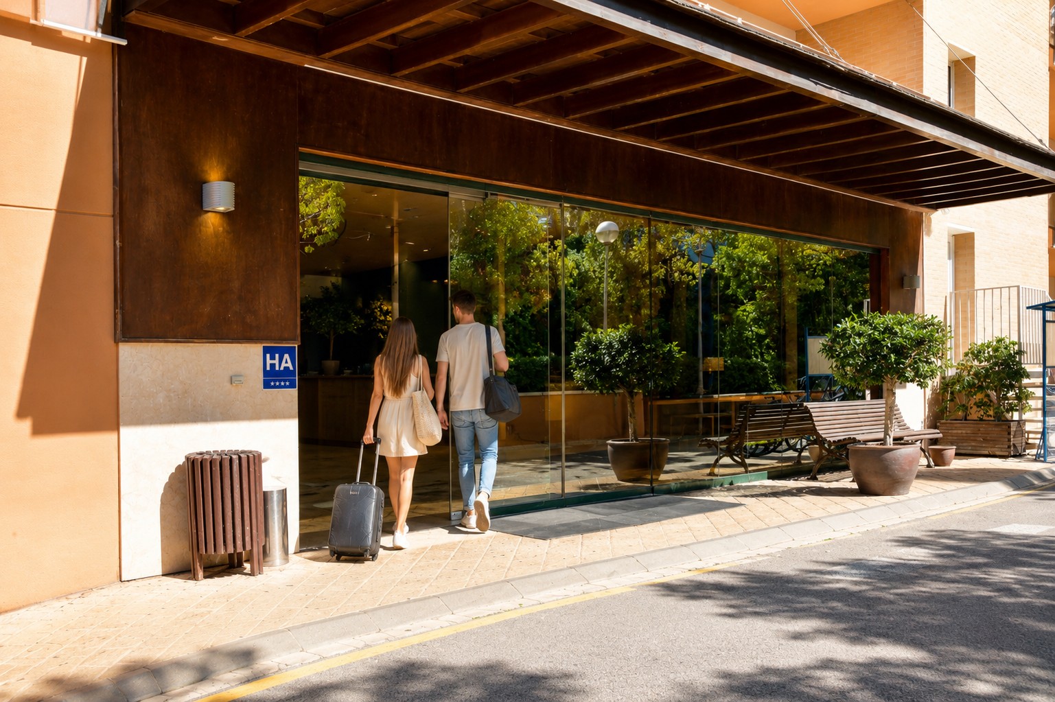 Dos personas caminan por el acceso exterior junto a una entrada con puerta de cristal y bancos de madera.