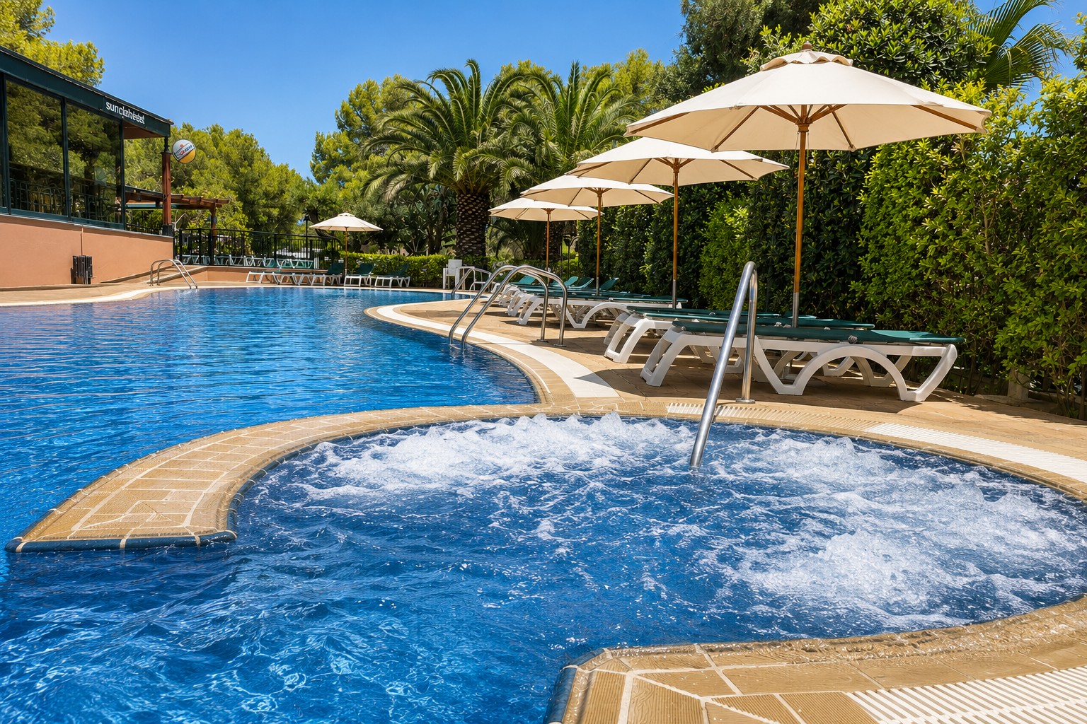 Jacuzzi exterior con chorros de agua junto a una piscina al aire libre y tumbonas bajo sombrillas.