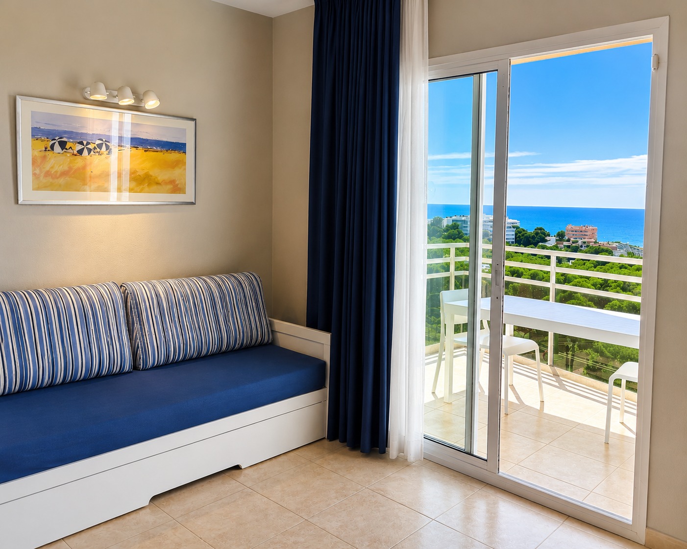 Se ve un dormitorio con un sofá, cortinas oscuras y una puerta de balcón con vistas al mar.