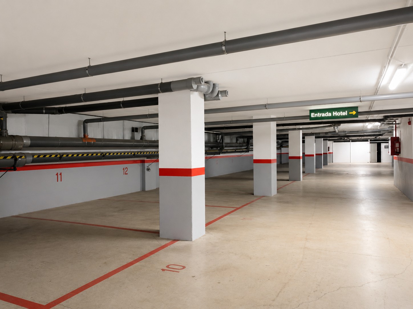 Alt: describe un aparcamiento interior con plazas señalizadas y columnas blancas con franjas rojas.