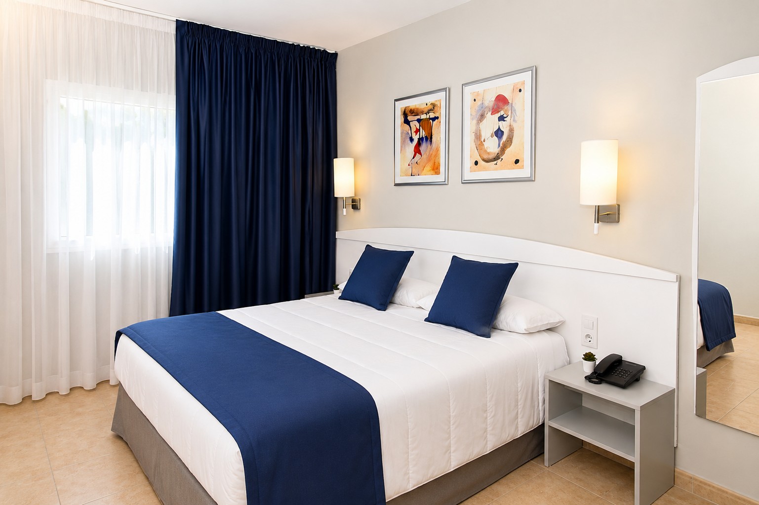 Se ve una cama doble con ropa de cama blanca y cojines azules, junto a mesita y lámparas de pared.