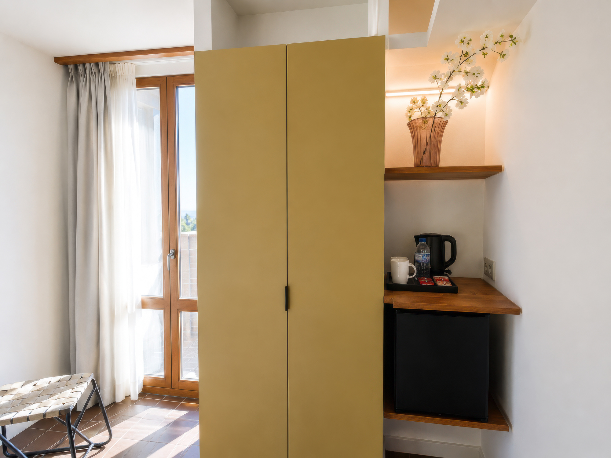 Se ve un armario y un pequeño área de cocina con cafetera y hervidor junto a una ventana con cortinas.