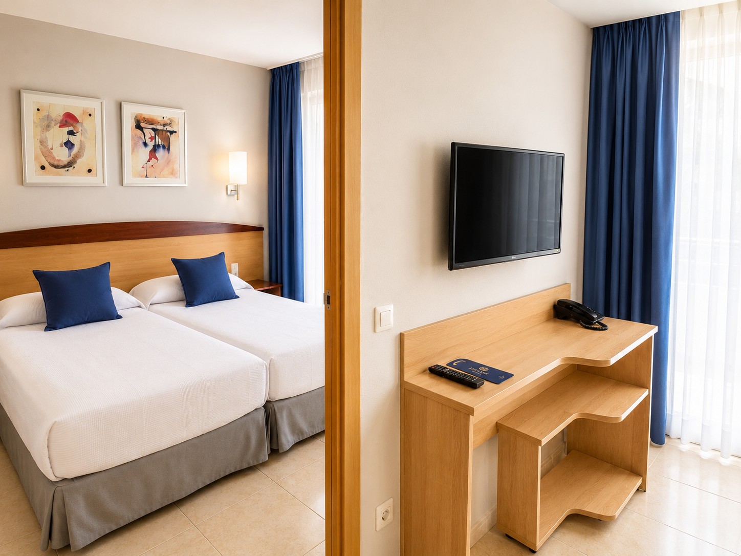 Se ve una cama con cojines, una televisión de pantalla plana y un escritorio de madera en una habitación con cortinas azules.