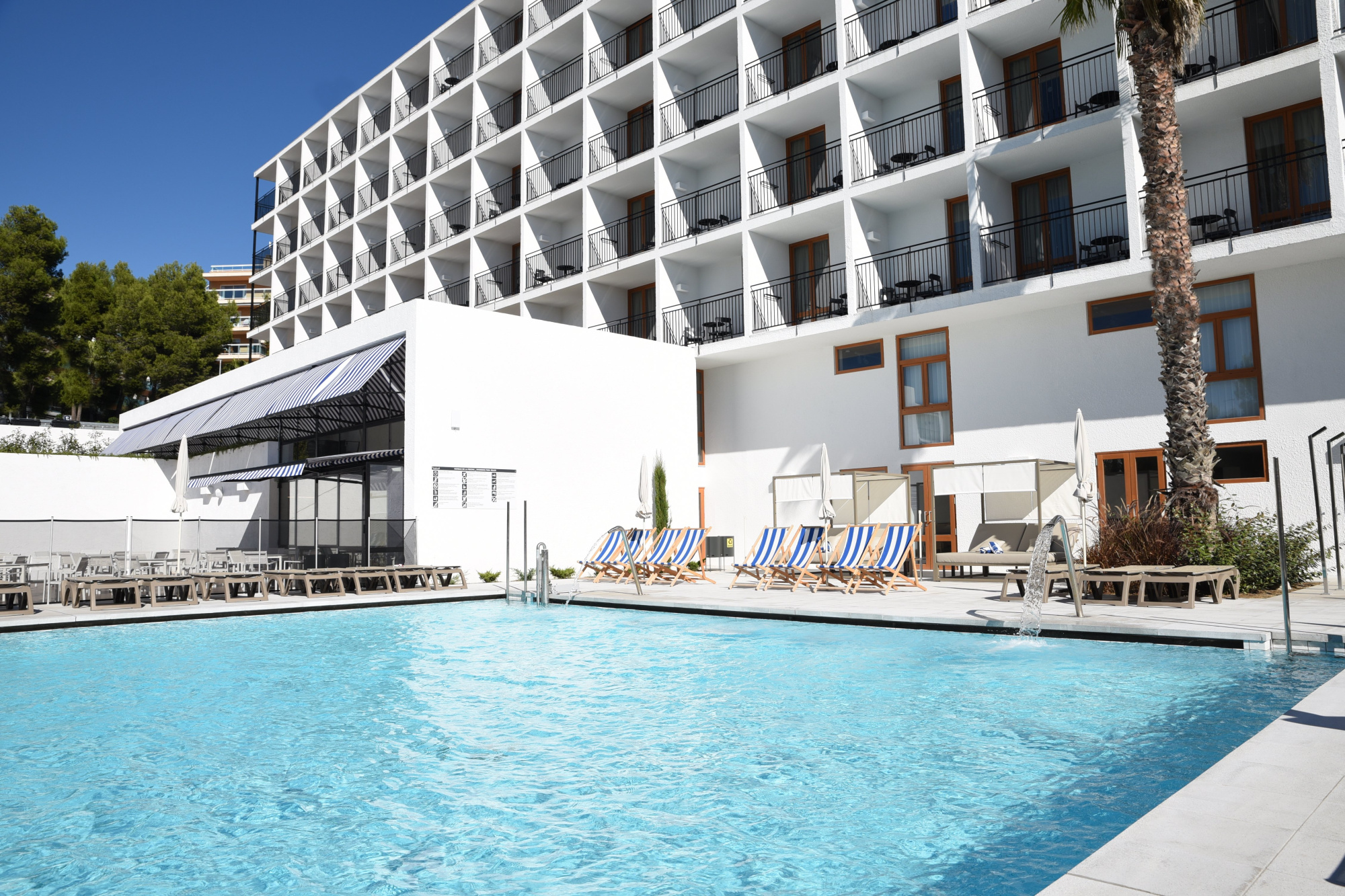 Área de piscina del SunClub Calavinya, con una piscina grande y zonas de descanso, rodeada de vegetación y mobiliario de exterior.