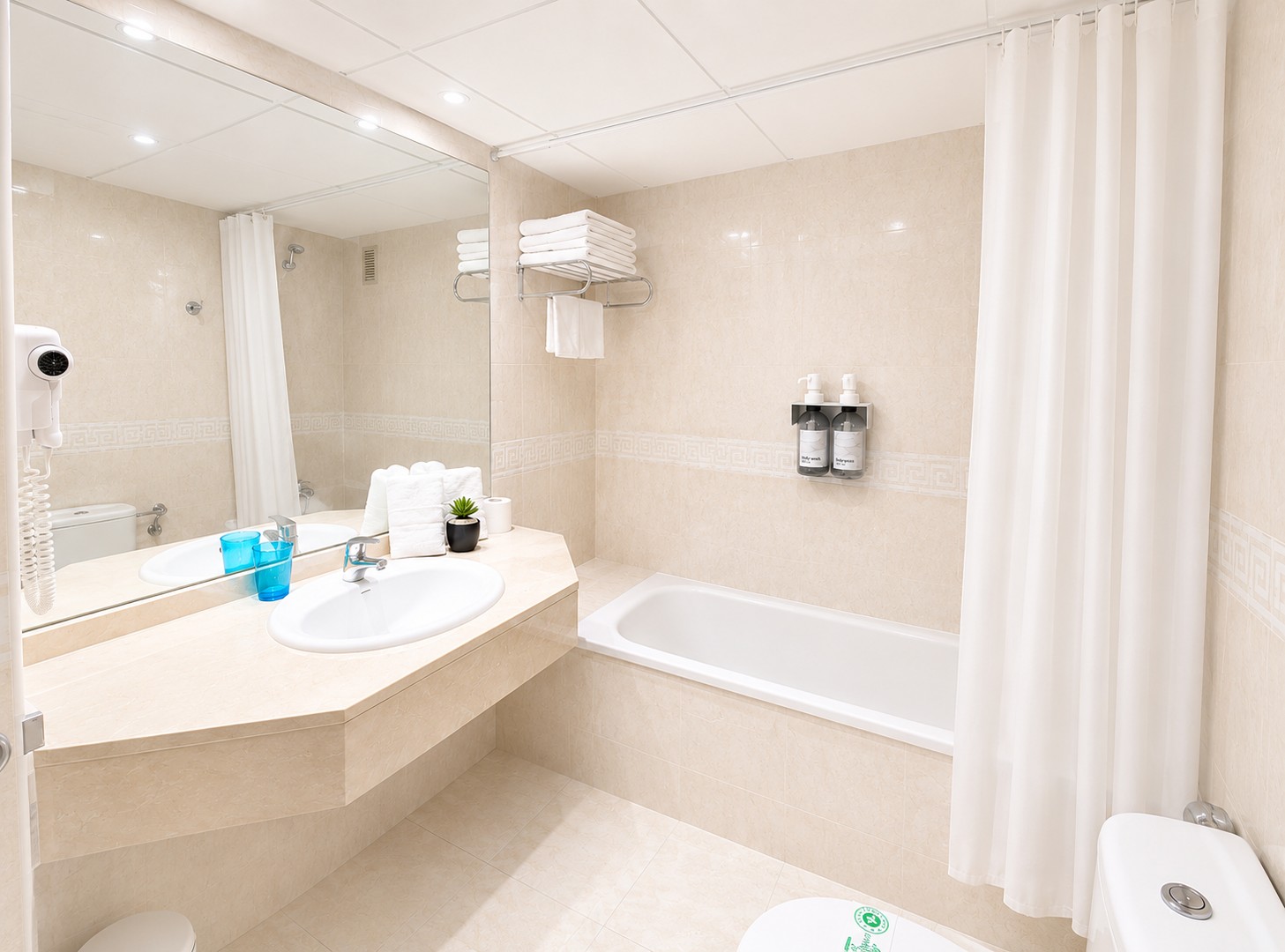 Se ve un baño luminoso con bañera, lavabo doble y cortinas de ducha blancas.