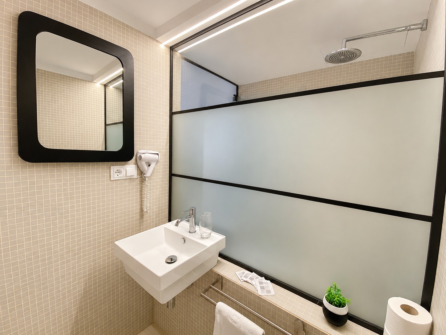 Se ve un baño con lavabo blanco, espejo con marco oscuro y mampara de ducha.