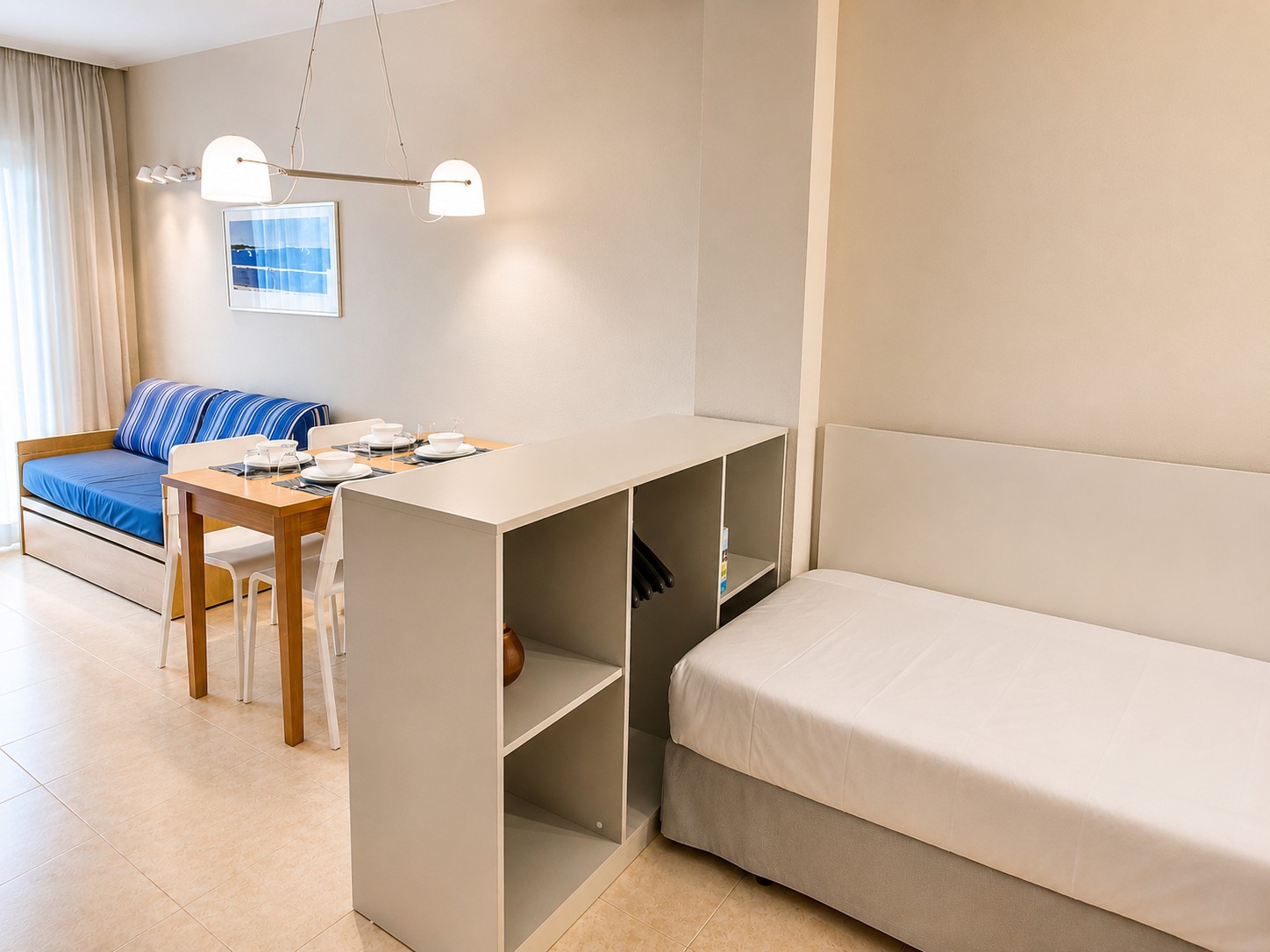 Se ve una zona de estar con sofá, mesa auxiliar y una silla junto a una pared con estantería abierta.