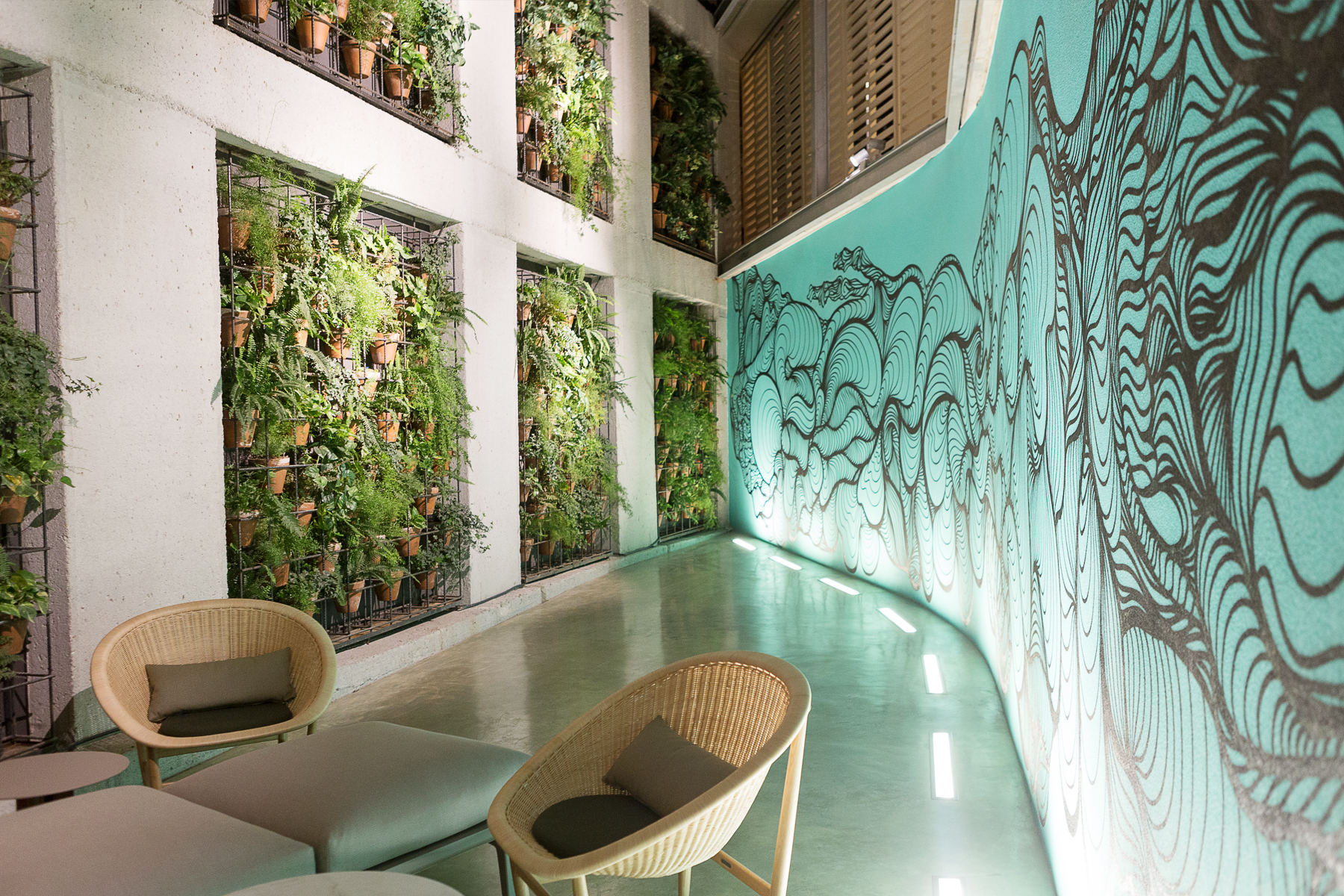 Se ve un pasillo interior con sillas de mimbre y un mural verde en la pared.