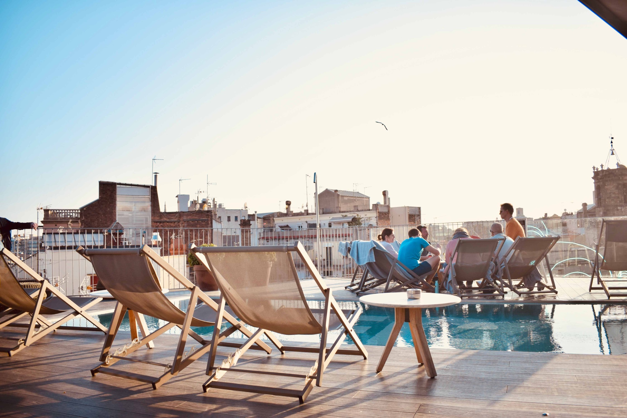 Terraza con piscina y tumbonas de madera junto a una mesa redonda.