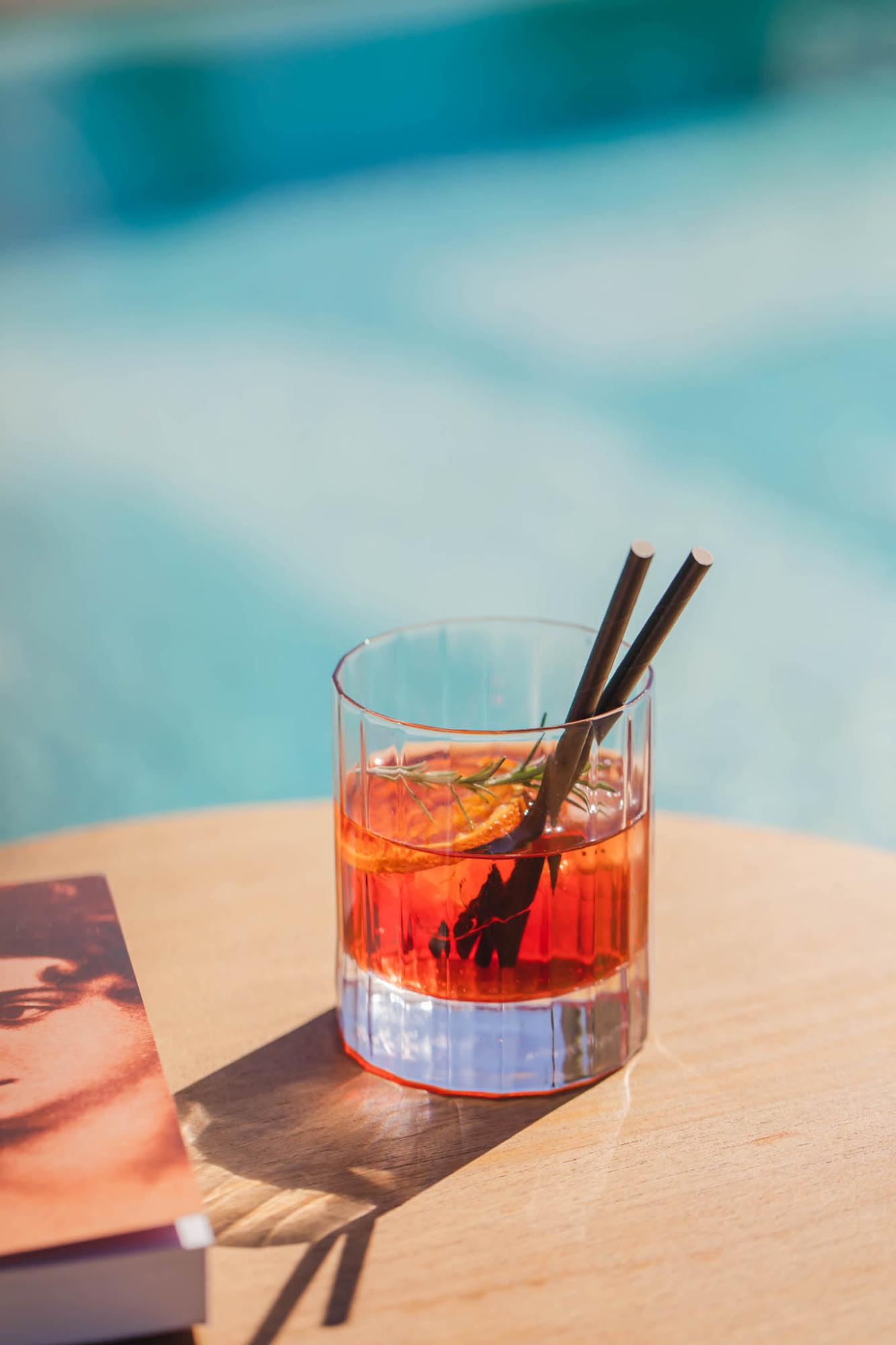 Hay un vaso con bebida roja y hielo sobre una mesa junto a una revista.