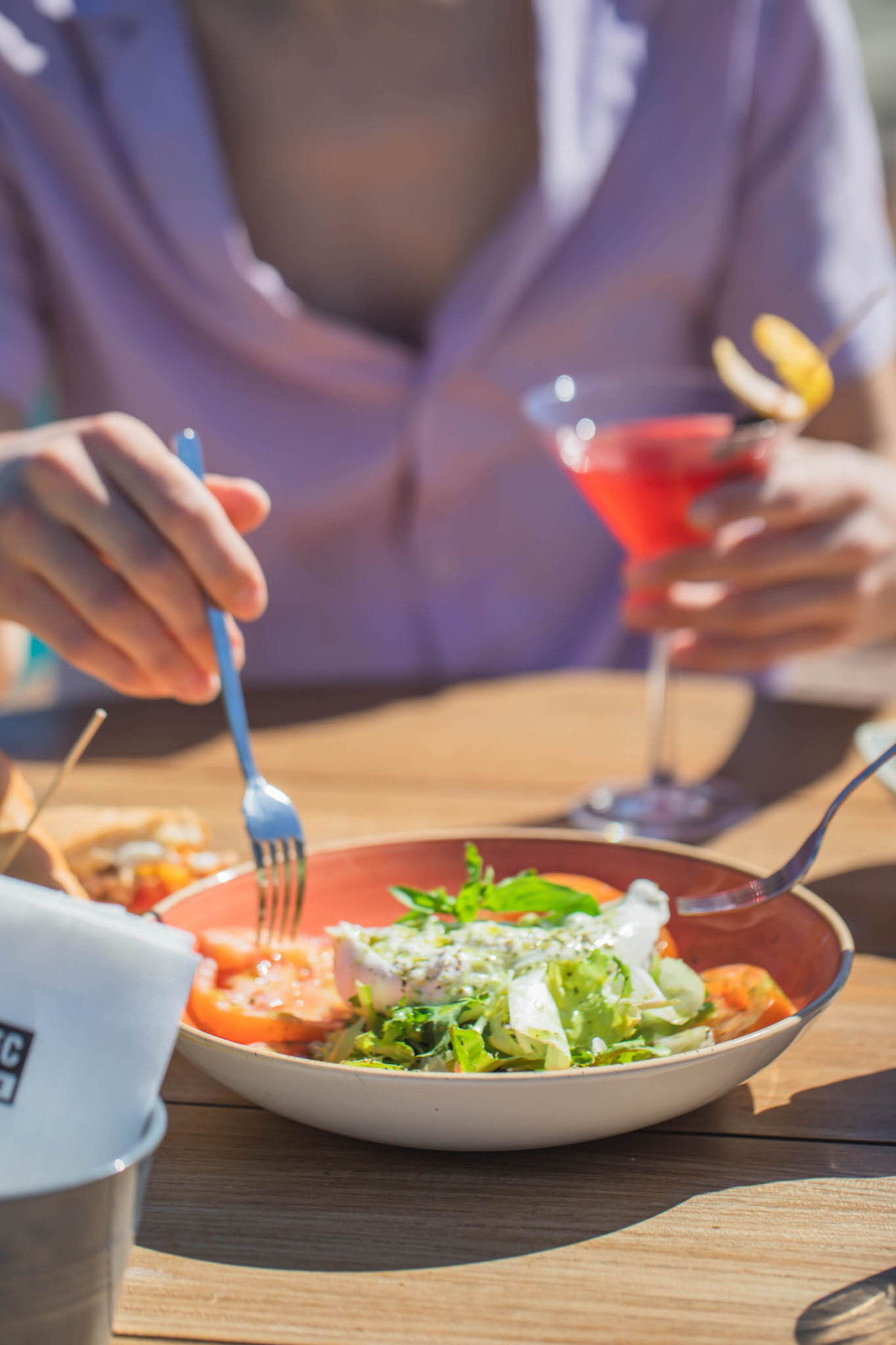 Una persona sirve ensalada en un plato sobre una mesa al aire libre.