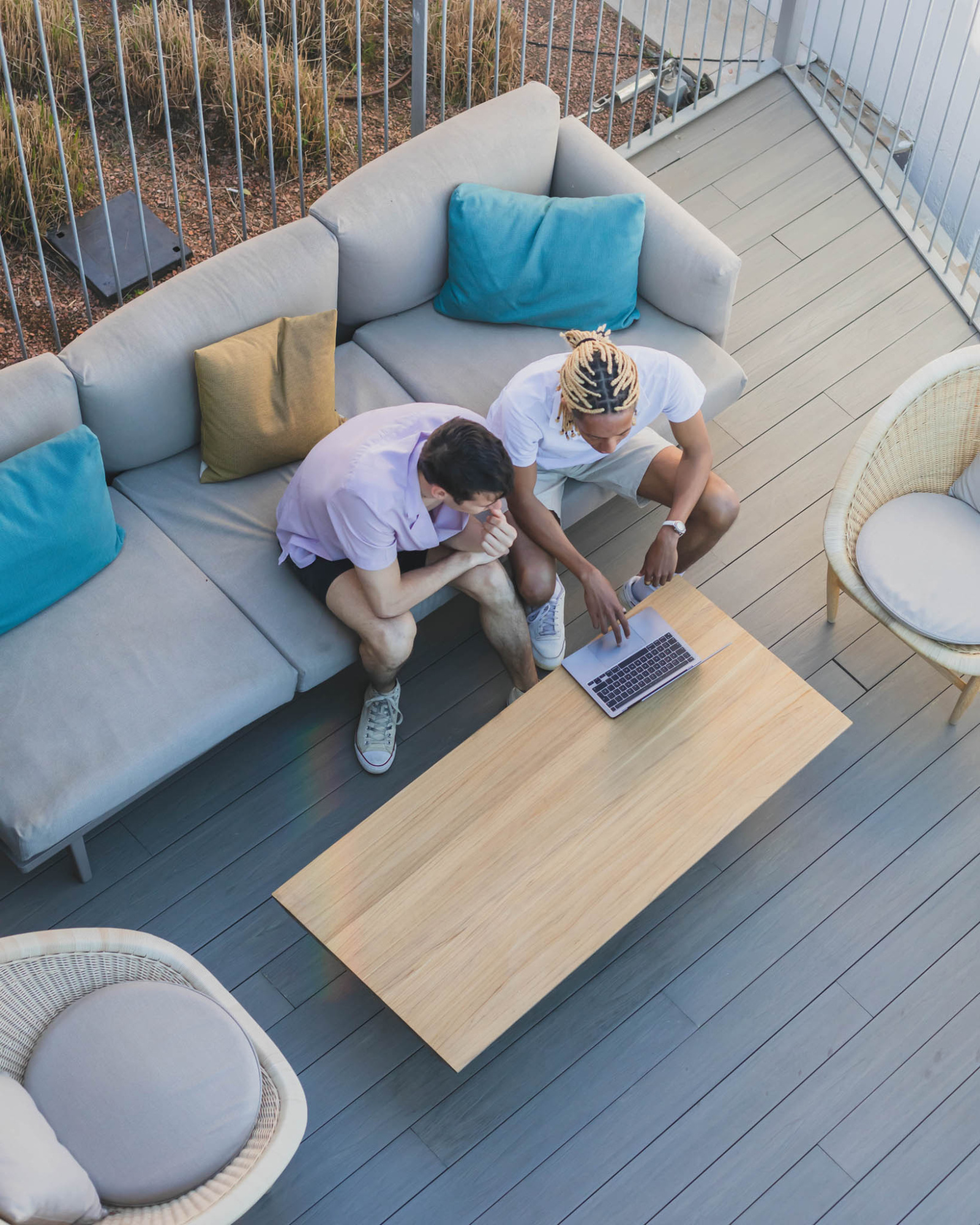 Dos personas se sientan en un sofá en una terraza con cojines y una mesa de madera.